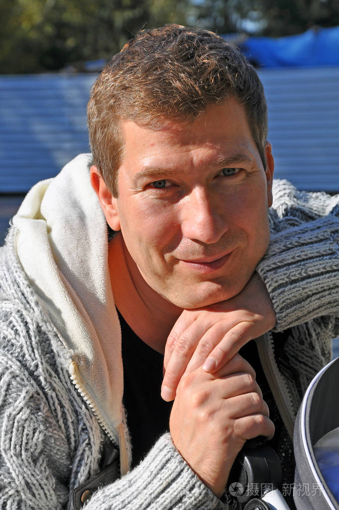 阳光明媚的一天,一位身穿灰色毛衣,双臂交叉的,面带