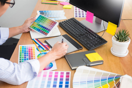在工作室或办公室，设计师编辑在办公桌旁的电脑上用绘图板和调色板绘制一个新项目