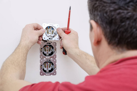 电工手拿插座在工艺安装或修理使用螺丝刀。 白色背景特写视图