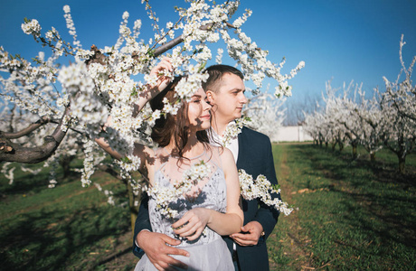 新婚夫妇在春暖花开的花园里散步时，新娘和新郎穿着一件轻便的衣服，温柔的感情