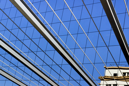 梁和钢索的图形线条，结合巴西里约热内卢金融中心的一座玻璃建筑的窗户。 强烈的蓝天和一座旧房子倒映在窗户上。 2017