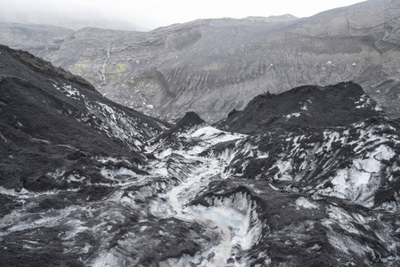 冰岛的Solheimajokull冰川显示冰上的灰烬堆和一条小溪流。