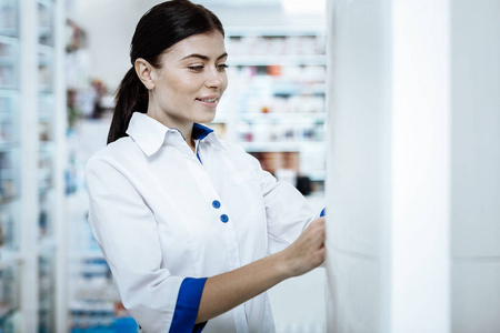可爱的微笑的年轻女子在一个白色的外套检查药店显示的情况下