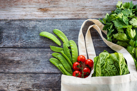 带有新鲜有机蔬菜和沙拉的生态购物袋，木制背景，俯视平面
