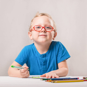 那个男孩戴着眼镜坐在桌子旁画画。