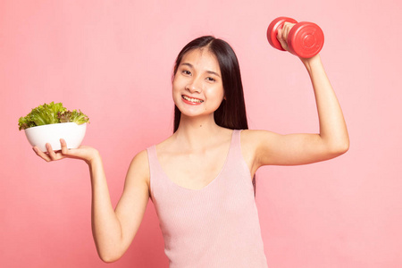 健康的亚洲女人，带哑铃和粉红色背景的沙拉