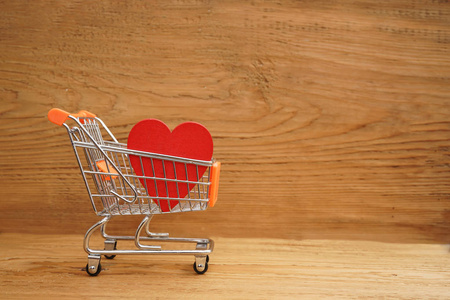 侧面观看红色心形装饰与迷你购物车在棕色木桌背景。 热爱浪漫购物和情人节假期的概念。 2月14日。