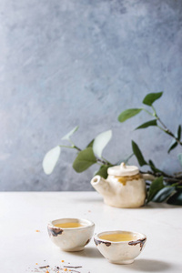 热绿茶在两个传统的中国粘土陶瓷杯和茶壶站在白色大理石桌子上。 背景上有绿色的树枝。