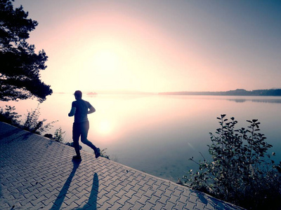 日出或日落时在湖岸人行道上奔跑的男人健康的生活方式观念照片