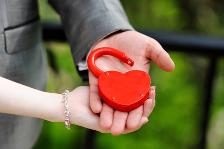 新娘和新郎的手把红锁保持在心脏的形式。 新婚夫妇把象征永恒爱情的锁挂在婚礼上。 结婚传统。