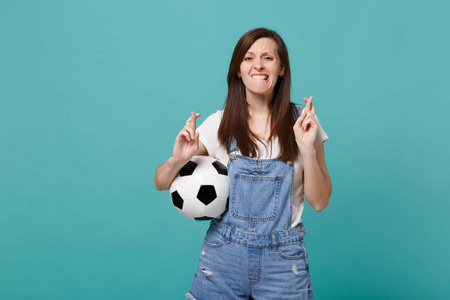 女球迷支持最喜欢的球队与足球等待片刻，手指交叉咬唇孤立在蓝色绿松石背景。 家庭休闲的概念