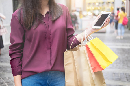 女人在商场里拿着纸袋看手机，一边享受一天的购物