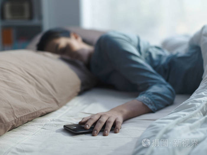 手里拿着智能手机睡觉的年轻