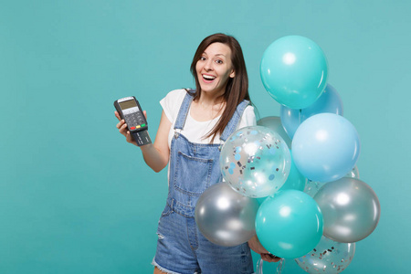 兴奋的女人持有无线现代银行支付终端，以处理获得信用卡支付，彩色气球隔离在蓝色绿松石背景。 生日派对情感观念