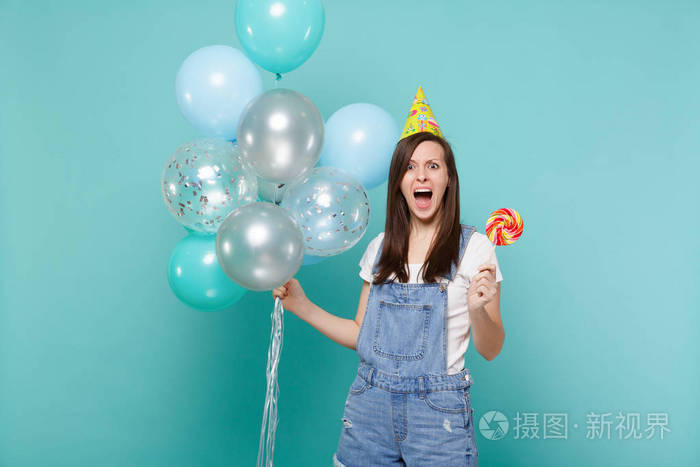 愤怒的尖叫的女人穿着牛仔服装生日帽拿着圆形的棒棒糖用蓝色绿松石
