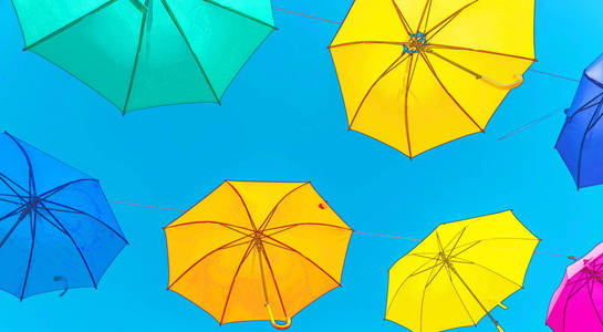 五颜六色的雨伞，城市街道装饰。 在蓝天上悬挂着五颜六色的雨伞