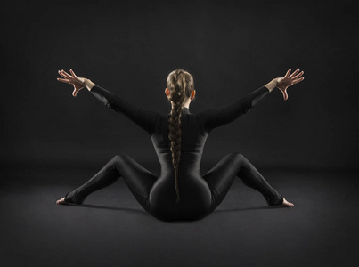 穿着黑色西装长发的女孩做体操。 演播室拍摄在黑暗的背景上。