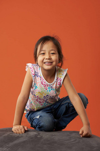 亚洲女孩微笑坐在橙色背景的沙发上的肖像