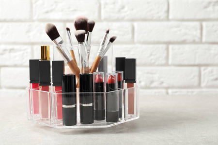 口红支架与不同的化妆产品在桌子上靠砖墙。 文本空间