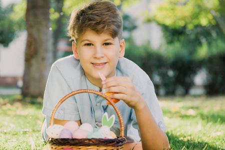 复活节快乐 可爱的微笑男孩少年穿着蓝色衬衫，在春天公园的草地上拿着手工制作的彩色鸡蛋。 花园里复活节庆祝活动彩蛋狩猎装饰