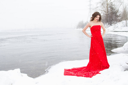 穿着红色衣服的年轻女孩站在雪覆盖的河岸上