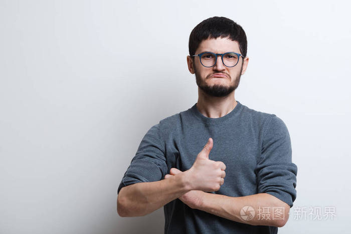 自信的年轻人的肖像显示竖起大拇指, 在白色背景.戴眼镜和灰色毛衣