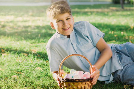 复活节快乐 可爱的微笑男孩少年穿着蓝色衬衫，在春天公园的草地上拿着手工制作的彩色鸡蛋。 花园里复活节庆祝活动彩蛋狩猎装饰