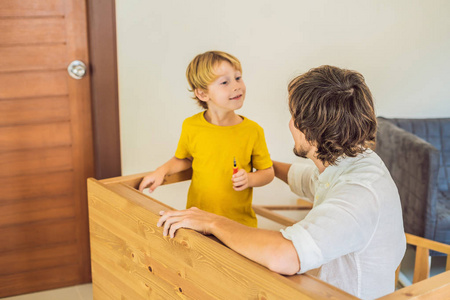 父子组装家具。男孩在家里帮助他的爸爸。快乐的家庭概念