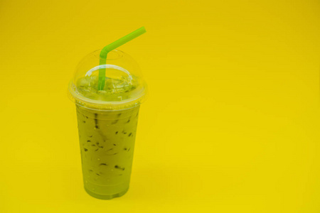 绿茶拿铁与冰在塑料杯子和秸秆在女性手与黄色修指甲在黄色背景。自制的冰抹茶拿茶与牛奶带走