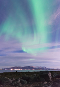 在冰岛雷克雅未克外的黑色沙滩海洋和山脉上的绿色北极光漩涡