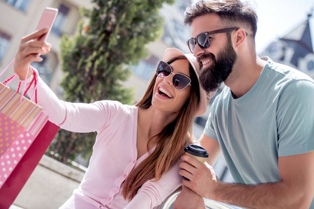 快乐夫妇自拍与智能手机与购物袋在城市。