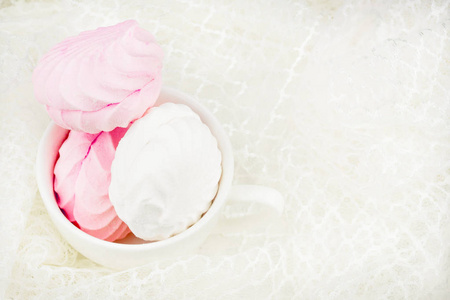 白色杯子和嫩棉花糖。 白色和粉红色棉花糖在一个白色花边背景的碗里。 头巾上温和的花边背景。 有地方签字