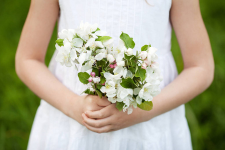 可爱的年轻女孩拿着一束苹果花。 美丽的女孩穿着白色的裙子在花园里，有着耀眼的苹果树。