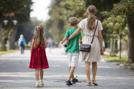在温暖的夏天,年轻的金发女子带着两个孩子,小女儿和儿子沿着阳光明媚