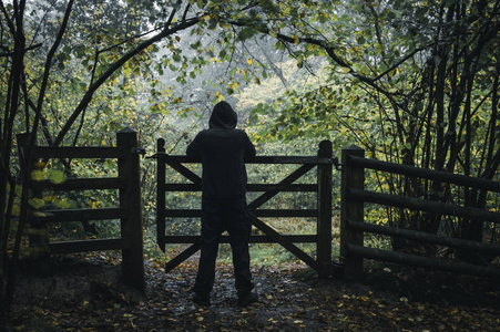 秋天, 一个孤独的头戴头套的身影站在森林的大门旁照片