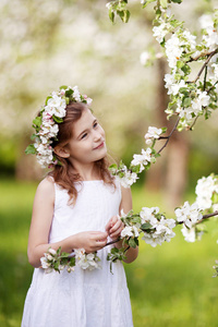 美丽的年轻女孩穿着白色的连衣裙在花园里，绿树成荫。可爱的女孩拿着苹果树树枝