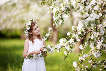 美丽的年轻女孩穿着白色的连衣裙在花园里，绿树成荫。可爱的女孩拿着苹果树树枝