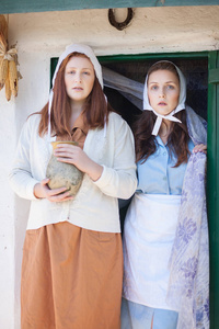 两个年轻的女人在一个复古的农村家庭的背景下，手里拿着一个水壶。