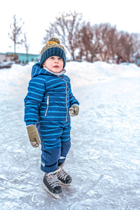 一个小男孩是一个35岁的孩子。冬天在城市公园里滑冰。溜冰场上的第一步。文本的可用空间。穿着蓝色工作服, 戴着暖和的帽子, 戴着