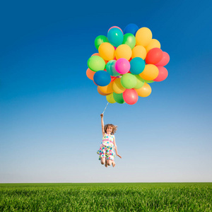 快乐的孩子在户外玩明亮的多色气球。 在蓝天背景下在绿色春天的田野里玩得很开心。 健康和积极的生活方式观念