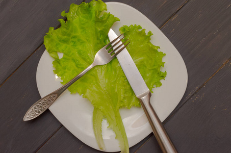 带叉子和刀的白色盘子上的沙拉叶。灰色木制背景。健康饮食的概念