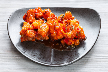 韩式中国菜上方的Kkanpunggi麻辣蒜蓉炒鸡片与蔬菜在甜酱的黑盘上特写