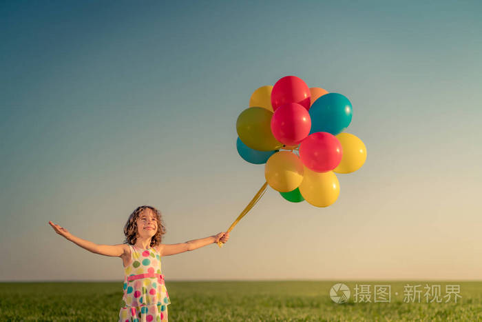 快乐的孩子在户外玩明亮的多色气球。 在蓝天背景下在绿色春天的田野里玩得很开心。 健康和积极的生活方式观念