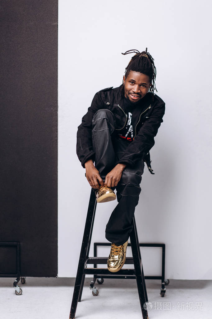 一个迷人的微笑黑人穿着黑色夹克穿着灰色背景的黑色裤子