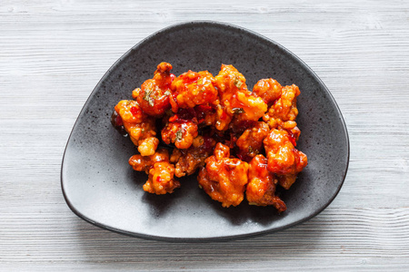 韩式中国菜顶上观Kkanpunggi辣炒鸡片，灰色桌子上的黑盘上有糖醋酱蔬菜