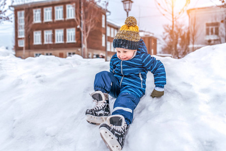 小男孩孩子35岁。堆满雪的积雪, 溜冰鞋城市公园的冬天。溜冰场上的第一步。文本的可用空间。穿着蓝色工作服和温暖的帽子, 手套。