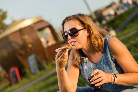 快乐的年轻女子在公园户外的包厢座位上拿着热比萨饼
