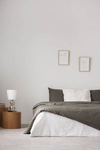 灯在木凳旁边的床白色最小卧室内部与海报。 真实照片