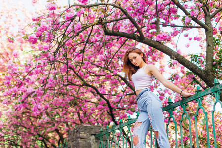 那个穿着时髦衣服的女孩在篱笆前摆姿势，看着她的花树上的镜头。