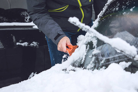 在降雪期间，人们用刷子和刮刀工具从雪和冰中清洗汽车。 冬季紧急情况。 天气相关的车辆紧急情况。 覆盖着雪的汽车